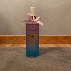 Pretty & Sexy body mist från Women'secret - Jag säljer en söt body mist i en cylinderformad flaska med färgskiftning från lila till blå. Flaskan har en rosa rosett vid halsen och gulddetaljer vid spraymunstycket. Doften heter Pretty & Sexy och etiketten är guldfärgad. Den är använd 1 gång men passade inte min doft på mig.