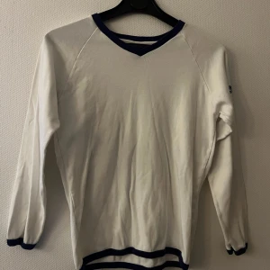 Vit långärmad tröja från Diesel Jeans - Vit långärmad tröja från Diesel Jeans med blåa detaljer vid hals, ärmslut och nederkant. Tröjan har en klassisk passform och är tillverkad i mjukt bomullsmaterial. Diesel Jeans-logga i blått på ärmen. Storlek L men liten i storleken