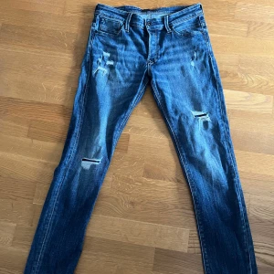 Blå slitna jeansbyxor från jack&jones - Säljer ett par blå jeansbyxor från jack&jones med slitningar och hål på benen. Perfekta för en avslappnad och trendig look. Modelln heter JJIGLENN och storlek 31/32