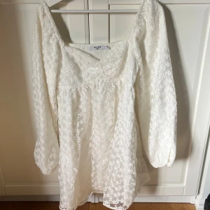 Vit långärmad spetsklänning från NA-KD, Studentklänning -  vit klänning från NA-KD med lång ärm och söt spetsdetalj över hela plagget. Klänningen har en lätt v-ringad halsringning och en luftig passform som ger en drömmig känsla.
