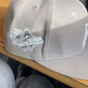Grå LA-keps med broderad logga st 58.7cm - Säljer en grå keps från New Era med vit broderad LA-logga framtill och World Series-märke på sidan. Klassisk modell bra skick och passar bra till street were 