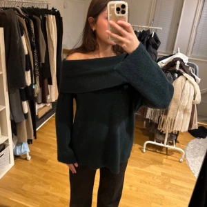 Mörkgrön offshoulder stickad tröja - Säljer en mörkgrön stickad tröja med bred offshoulder-krage. Tröjan har lång ärm och en avslappnad passform, perfekt för att ge en cool och trendig look.