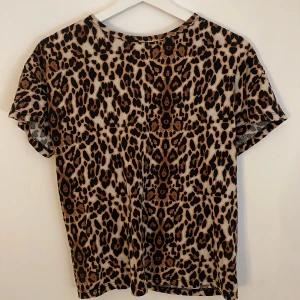 Leopardmönstrad blus XS/S - Säljer en kortärmad blus med leopardmönster i bruna, svarta och beige toner. Toppen har rund halsringning och är tillverkad i ett lätt och mjukt material som känns skönt mot huden. Perfekt för dig som vill sticka ut med ett djurmönster. Tröjan är sydd förhand på ryggen.