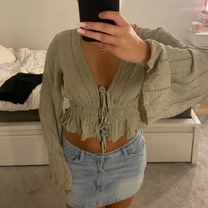 Ljusgrön blus med snörning och volang - Supersöt ljusgrön blus med v-ringning, långa vida ärmar och snörning framtill. Toppen har volangkant nedtill och ett luftigt, lätt material med broderade detaljer. Köpt för över ett år sedan och får ingen användning av den längre😊