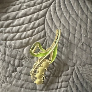 Blommig hårklämma i guld och grönt - Superfin hårklämma i form av en blomma med guldiga detaljer och ljusgröna blad. Klämman har en elegant och unik design som verkligen sticker ut och ger en cool touch till din frisyr. Perfekt accessoar för att lyfta vilken look som helst.