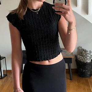 Svart croppad topp med struktur - Säljer en svart croppad topp med snygg struktur och lätt vågiga kanter från Zara i nyskick. Toppen har korta ärmar och en enkel, stilren look som passar perfekt till höga jeans eller kjol. 