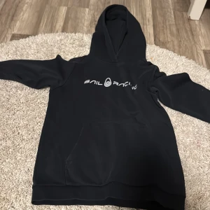 Svart Sail Racing hoodie med tryck - Svart hoodie från Sail Racing med vit logga på bröstet. Klassisk känguruficka framtill och stor huva. Tröjan har lång ärm och är gjord i mjukt material som känns skönt mot huden. Perfekt för dig som gillar sportig och clean stil.