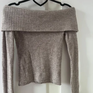Beige ribbad offshoulder stickad tröja - Superfin beige stickad tröja med ribbat mönster och bred offshoulder-krage. Långärmad och mjuk.