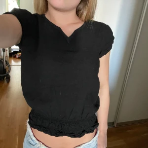 Svart kortärmad blus med resår - Svart blus med korta ärmar och v-ringning. Toppen har resår och volangdetalj i nederkanten som ger en snygg croppad look. Storlek 164 men passar mig som använder xs/s!!🥰