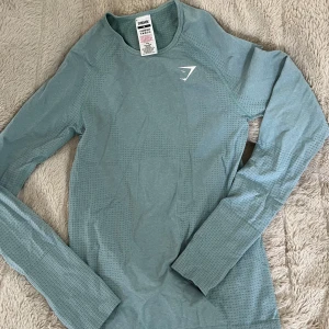 Blå långärmad träningströja Gymshark - Superskön mjuk, blå långärmad träningströja från Gymshark med diskret mönster. Tröjan är i stretchigt material, perfekt för gymmet eller löprundan. Sitter lagom tight. 