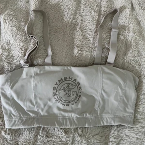 Beige linnetopp från Gymshark - Snygg beige linnetopp från Gymshark med justerbara axelband och tryckt logga framtill. Tillverkad i ett stretchigt och mjukt material som passar perfekt för träning. Använd en gång.