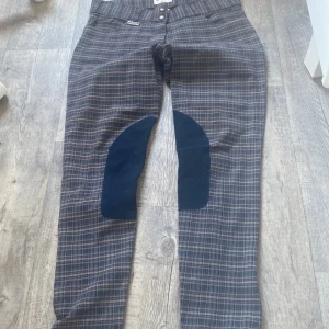 Rutiga ridbyxor från Back 2 Back - Snygga rutiga ridbyxor från Back 2 Back i grått och blått med förstärkta knäpartier i mörkblå mocka. Klassisk passform med två knappar i midjan och diskret logga. Perfekta för dig som gillar stilrena ridkläder med lite edge.