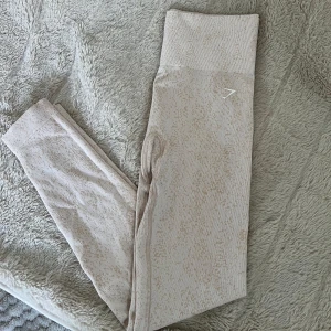 Beige mönstrade leggings från Gymshark - Säljer ett par snygga beige leggings från Gymshark med diskret mönster och hög midja. De är tillverkade i en mjuk och stretchig blandning av nylon, polyester och elastan, perfekta för träning eller chill. 