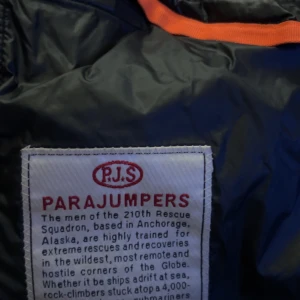 Svart dunväst från Parajumpers - Säljer en svart dunväst från Parajumpers med quiltad framsida och sidor i stretchigt material. Västen har orange detaljer på insidan och dragkedja framtill. Perfekt för lager-på-lager och riktigt snygg till streetwear eller outdoor-stil.