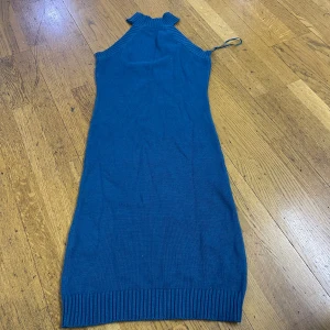 Blå stickad klänning Gina Tricot - Snygg blå stickad klänning från Gina Tricot med ribbade detaljer vid hals och ärmhål. Ärmlös modell med hög hals och rak passform. Perfekt för dig som gillar en enkel men trendig look.