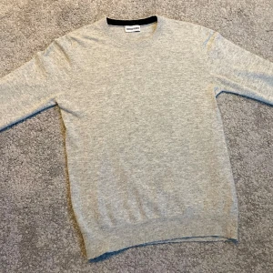 Marken Weber cashmyr tröja - En stilren ljusgrå cashmyr från Marken Weber. Tröjan har rund halsringning, ribbade muddar och är långärmad. Perfekt för lager-på-lager och enkel att matcha med jeans eller chinos.