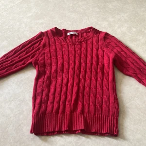 Röd kabelstickad tröja från Gina Tricot - Säljer en röd kabelstickad tröja från Gina Tricot i storlek XS. Tröjan har rund halsringning, långa ärmar och breda ribbade muddar vid ärmslut och nederkant. Perfekt för dig som gillar klassisk och mysig stil.