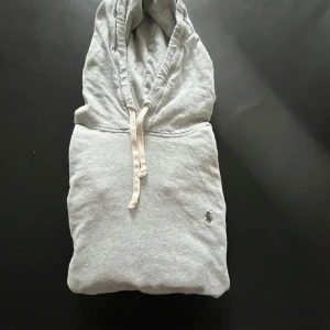 Grå hoodie från Polo Ralph Lauren - Snygg ljusgrå hoodie från Polo Ralph Lauren med klassisk broderad logga på bröstet. Tröjan har huva med snörning, känguruficka och långa ärmar. Perfekt för chill dagar eller när du vill ha en clean och enkel stil.