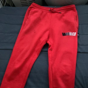 Röda mjukisbyxor från Hoodrich L - Röda mjukisbyxor från Hoodrich i storlek L. Byxorna har broderad logga i svart, grått och vitt på ena benet, snörning i midjan och två sidofickor. Perfekta för chill eller streetwear. Mjukt material som känns skönt mot huden. 
