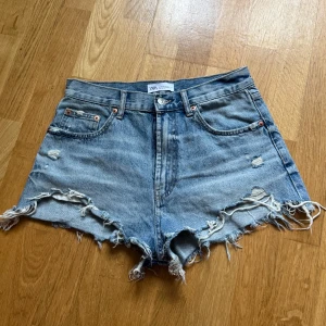Jeansshorts Zara - Jeansshorts från Zara med hög midja och råa, fransiga kanter. Shortsen har slitna detaljer både fram och bak, med en dragkedja framtill. Perfekta för sommaren!😇