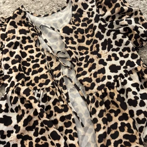 Leopardmönstrad kort blus med snörning - Snygg kort blus med leopardmönster i beige, svart och bruna toner. Blusen har korta puffärmar och snörning framtill för en cool detalj. Tillverkad i ett lätt och luftigt material som känns skönt mot huden.