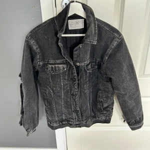 Svart jeansjacka med råa detaljer - Cool svart jeansjacka från H&M Studio med råa, slitna detaljer och unik söm på ryggen. Jackan har klassisk krage, knappar framtill och fickor på bröstet och sidorna. Perfekt för dig som gillar en edgy streetstyle-look.