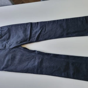 Mörkblå jeans från Nudie Jeans Co - Snygga svarta jeans från Nudie Jeans Co med klassisk femficksdesign och raka ben. Jeansen är tillverkade i mjukt denimtyg och har subtila detaljer som märkets logga på bakfickan och knappen. Perfekta för en clean och stilren look.