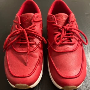 Röda Nike Air Max Thea Ultra sneakers strl 39 - Nike Air Max Thea Ultra sneakers i helrött skinn med matchande röda snören och vit sula. Klassisk Swoosh på sidan och Air Max-detalj i sulan. Snygg, sportig look och bekväm passform för hela dagen. Perfekt för dig som vill sticka ut med färg på fötterna.