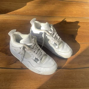 Nike Air Jordan 4 Pure Money sneakers - Säljer ett par Nike Air Jordan 4 Pure Money sneakers i helvitt skinn med silvriga detaljer och meshpaneler på sidorna. Klassisk chunky sula, snörning och ikoniska Air-detaljer. Perfekta för dig som vill sticka ut med stilrena och tidlösa sneakers.
