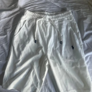 Vita shorts från Polo Ralph Lauren - Snygga vita shorts från Polo Ralph Lauren med klassisk broderad logga i mörkblått på benet. De har elastisk midja med snörning och är tillverkade i mjuk bomull.