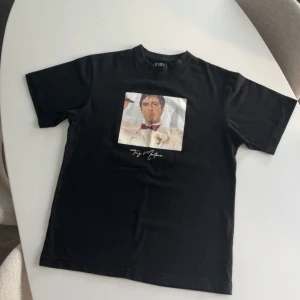 Svart Scarface T-shirt - Snygg svart T-shirt med ikoniskt Scarface-motiv. Köpt i Spanien och knappt tillgänglig i Sverige, vilket gör den till ett unikt fynd för fans av klassikern! ✅ Storlek: [S] ✅ Skick: Som ny, endast provad/använd ett fåtal gånger ✅ Material Perfekt för dig som gillar retrofilm, streetwear eller vill ha något som inte alla andra har!