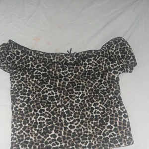 Leopardmönstrad offshoulder topp FB Sister - Säljer en snygg offshoulder topp från FB Sister i storlek L. Toppen har leopardmönster i svart, beige och brunt, med en liten rosett framtill och elastisk kant upptill. Perfekt för dig som vill sticka ut med ett djurmönstrat plagg.