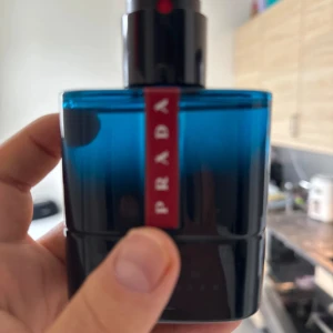 Prada Luna Rossa Blue parfym - Snygg parfymflaska från Prada Luna Rossa-serien i en djupblå glasdesign med svart och röd detalj. Flaskan har en modern, stilren form och känns lyxig i handen. Perfekt för dig som gillar exklusiva dofter och vill ha något som sticker ut i badrumshyllan.