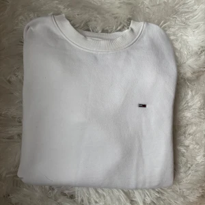 Vit sweatshirt från Tommy Hilfiger - Klassisk vit sweatshirt från Tommy Hilfiger med rund halsringning och diskret logga broderad på bröstet. Tröjan har långa ärmar och ribbade muddar vid ärmslut och nederkant. Perfekt för en clean och stilren look.