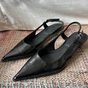 Svarta kittenheels - Snygga kitten heel klackar från Zara i glansigt lackmaterial med spetsig tå och låg klack. Skorna har öppen häl och smal rem med spänne runt ankeln.