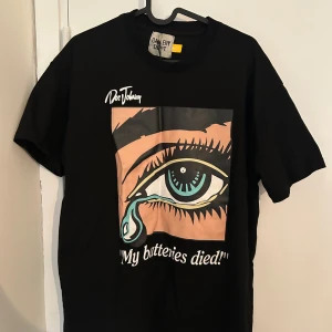 Svart Gallery Dept t-shirt med tryck - Svart t-shirt från Gallery Dept. x Doc Johnson med stort grafiskt tryck av ett öga och texten 'My batteries died!' på framsidan. Baksidan har färgglad text och logga. Klassisk passform och rund hals, tillverkad i mjuk bomull.