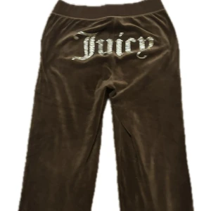 Bruna velourbyxor från Juicy Couture - Mysiga bruna velourbyxor från Juicy Couture med strassdetaljer och texten 'Juicy' på baksidan. Byxorna har dragsko i midjan och fickor framtill. Perfekta för en avslappnad och trendig look. Dm för fler bilder
