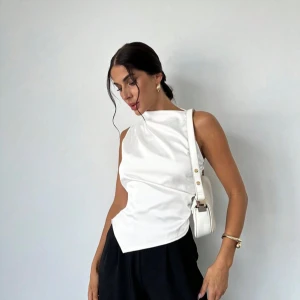 Vit ärmlös omlottopp - Snygg vit ärmlös topp med omlottdetalj och hög hals. Toppen har en elegant och stilren design som passar perfekt till många olika outfits. Materialet ser ut att vara mjukt och följsamt. Har Xs, S, M, L