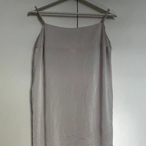 Ljusbeige axelbandslös klänning - Enkel och stilren ljusbeige klänning med smala axelband och rak passform. Klänningen är ärmlös och har en slät yta, perfekt för varma dagar eller sommarens tillfällen.