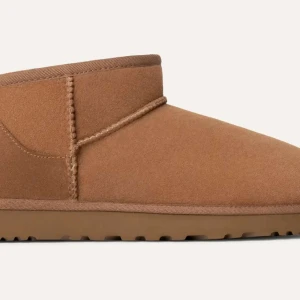 Bruna UGG boots med fårskinn - Klassiska bruna UGG boots i mocka med mjukt vitt fårskinnsfoder. Skorna har rund tå, platt sula och UGG-logga bak. Perfekta för kalla dagar och superbekväma att ha på sig.