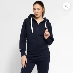 Mörkblå hoodie med dragkedja från russemerch - Snygg och bekväm mörkblå hoodie med dragkedja och vita snören. Storlek xs aldrig advent prislapp kvar. Perfekt för en avslappnad stil. Den har långa ärmar och en praktisk huva.