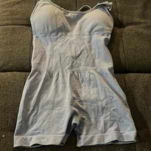 Ljusblå ribbad onesie med öppen rygg - Supersöt ljusblå onesie med smala axelband och ribbad struktur. Modellen har öppen rygg med snygga banddetaljer och korta ben. Perfekt för dig som vill ha något bekvämt och stilrent.