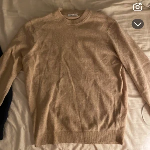 Beige stickad tröja från Zara - Säljer en stilren beige stickad tröja från Zara. Tröjan har rund halsringning och långa ärmar med ribbade muddar vid ärmslut och nederkant. Perfekt för lager-på-lager och enkel att matcha med olika outfits. Material: 100% ull. Nypris: 400-500 kr