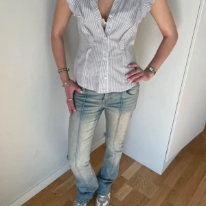 Ljusblå bootcut jeans med råa kanter - Säljer ett par ljusblå bootcut jeans med råa, fransiga benslut och markerade sömmar. Jeansen har klassiska bakfickor och en något utsvängd passform nertill. Perfekta för en avslappnad och trendig look.