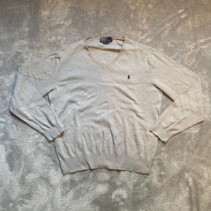 Beige v-ringad tröja från Polo Ralph Lauren - Säljer en stilren beige v-ringad tröja från Polo Ralph Lauren med den klassiska broderade loggan på bröstet. Tröjan är i mjukt material och har långa ärmar samt ribbade muddar vid ärmslut och nederkant. Bröstvidd ca 50 cm.
