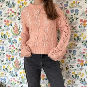 Ljusrosa stickad tröja med hålmönster - Superfin ljusrosa stickad tröja med hålmönster och breda ärmar. Tröjan har rund halsringning och ribbade muddar vid ärmslut och nederkant. Perfekt för lager-på-lager och ger en söt, trendig look. 
