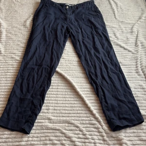 Mörkblå Linnebyxor från Kappahl - Säljer ett par mörkblå byxor från Kappahl i linne. Byxorna har normal passform, raka ben och klassisk midja med knapp och dragkedja. Perfekta för en avslappnad stil och passar perfekt till sommaren.