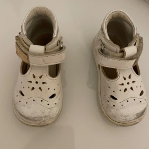 Vita sandaler från Kavat med kardborre - Säljer ett par vita sandaler från Kavat i skinn med kardborreknäppning. Skorna har fina utskurna detaljer på ovandelen och rund tå. Perfekta för små barn som vill ha bekväma och luftiga skor.