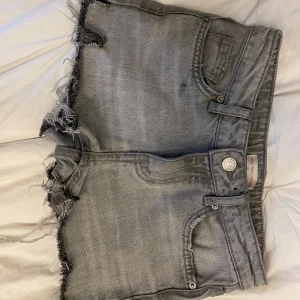 Grå jeansshorts med fransar - Säljer ett par grå jeansshorts med fransade kanter och klassisk femficksdesign. Shortsen har en avslappnad passform. Storleken är 140 cm. De är 34 cm rakt över midjan och ungefär 23 cm ner. Bra skick!