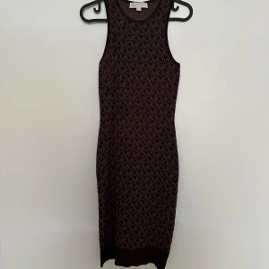 Svart och brun ärmlös klänning från Michael Kors - Säljer en snygg ärmlös klänning från Michael Kors i svart och brun med MK-mönster över hela plagget. Klänningen är figurnära och har rund halsringning. Perfekt för dig som gillar stilrena och trendiga plagg.